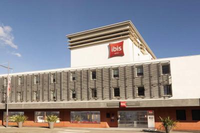Chambre d'hôtel lumineuse avec un lit double, une fenêtre avec rideaux rouges et un bureau en bois clair.