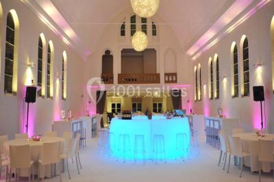 Salle de réception lumineuse avec bar central circulaire, tables hautes et éclairage coloré.