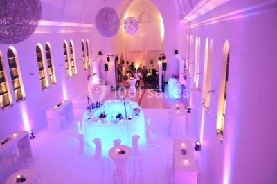 Salle de réception lumineuse avec bar central circulaire, tables hautes et éclairage coloré.