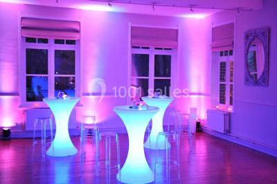 Salle de réception lumineuse avec bar central circulaire, tables hautes et éclairage coloré.