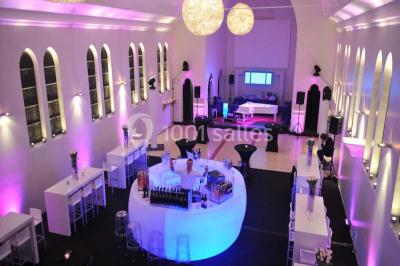 Salle de réception lumineuse avec bar central circulaire, tables hautes et éclairage coloré.