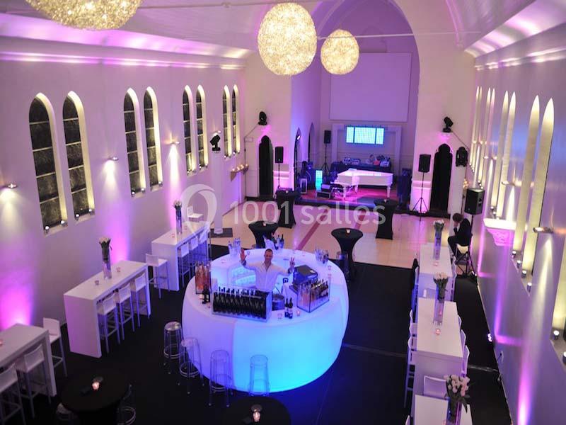 Salle de réception lumineuse avec bar central circulaire, tables hautes et éclairage coloré.