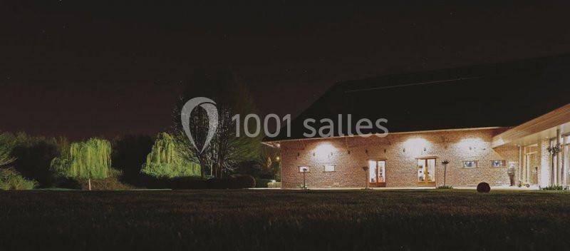 Bâtiment en briques éclairé la nuit, entouré d'arbres et d'une pelouse sombre.