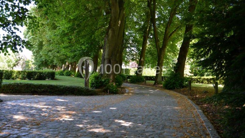 Allée pavée bordée d'arbres et de buissons dans un parc verdoyant, sous une lumière naturelle.