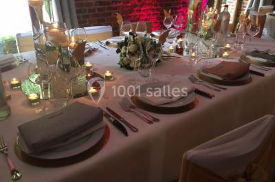 Table élégamment dressée avec nappes blanches, vaisselle raffinée, bougies allumées et décoration florale.