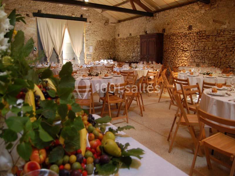 Salle de réception en pierre avec tables dressées, chaises en bois et décoration de fruits au premier plan.