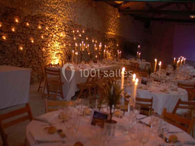 Salle de réception décorée avec des tables dressées, des chandeliers allumés et un éclairage chaleureux sur les murs en…