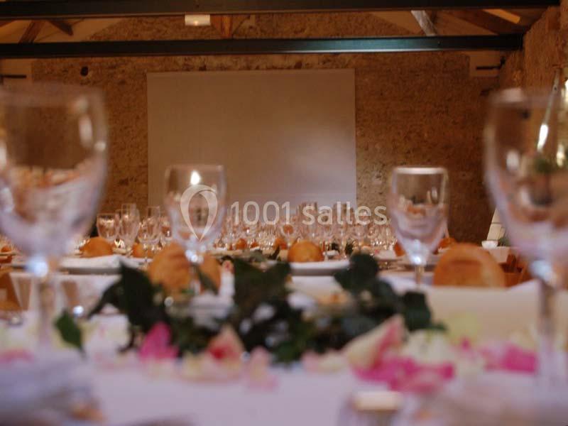 Salle de réception avec tables dressées, verres, pain et décoration florale, éclairée par une lumière douce.