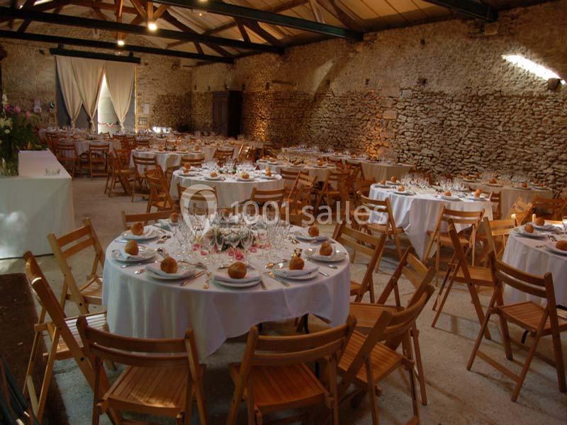 Salle en pierre avec des tables rondes dressées pour un repas, entourées de chaises en bois pliantes.