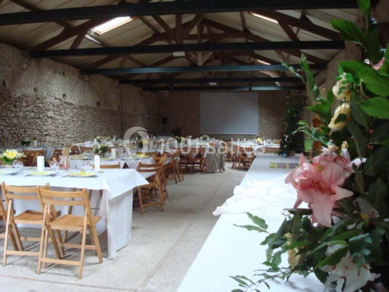 Salle de réception avec tables dressées, chaises en bois, murs en pierre et décoration florale au premier plan.