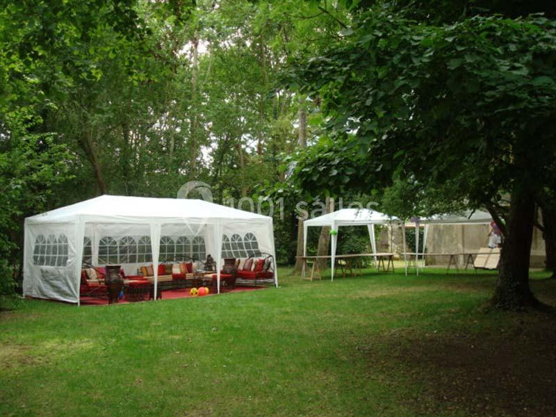 Deux tentes blanches installées dans un jardin verdoyant, avec des tables et des sièges visibles à l'intérieur.