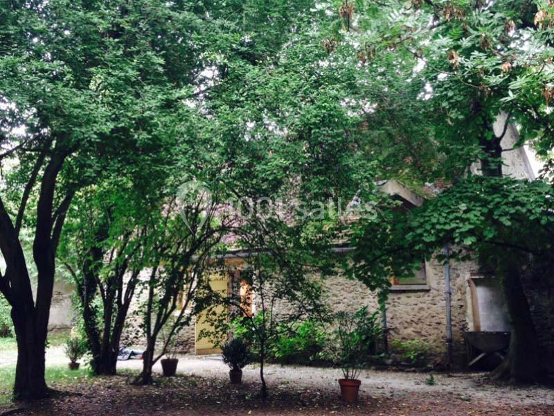 Maison en pierre entourée d'arbres et de végétation dense dans un jardin ombragé.