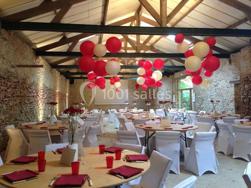 Salle de réception décorée avec des lanternes rouges et blanches suspendues, tables rondes dressées avec nappes blanches.