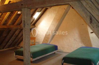 Deux lits simples avec couvertures vertes dans une chambre mansardée aux poutres apparentes et murs en plâtre.