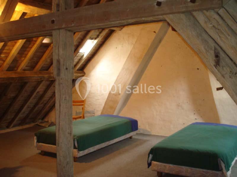 Deux lits simples avec couvertures vertes dans une chambre mansardée aux poutres apparentes et murs en plâtre.