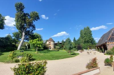 Jardin avec bancs, tables en bois et un pigeonnier en arrière-plan sous un ciel nuageux.