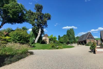 Jardin avec bancs, tables en bois et un pigeonnier en arrière-plan sous un ciel nuageux.