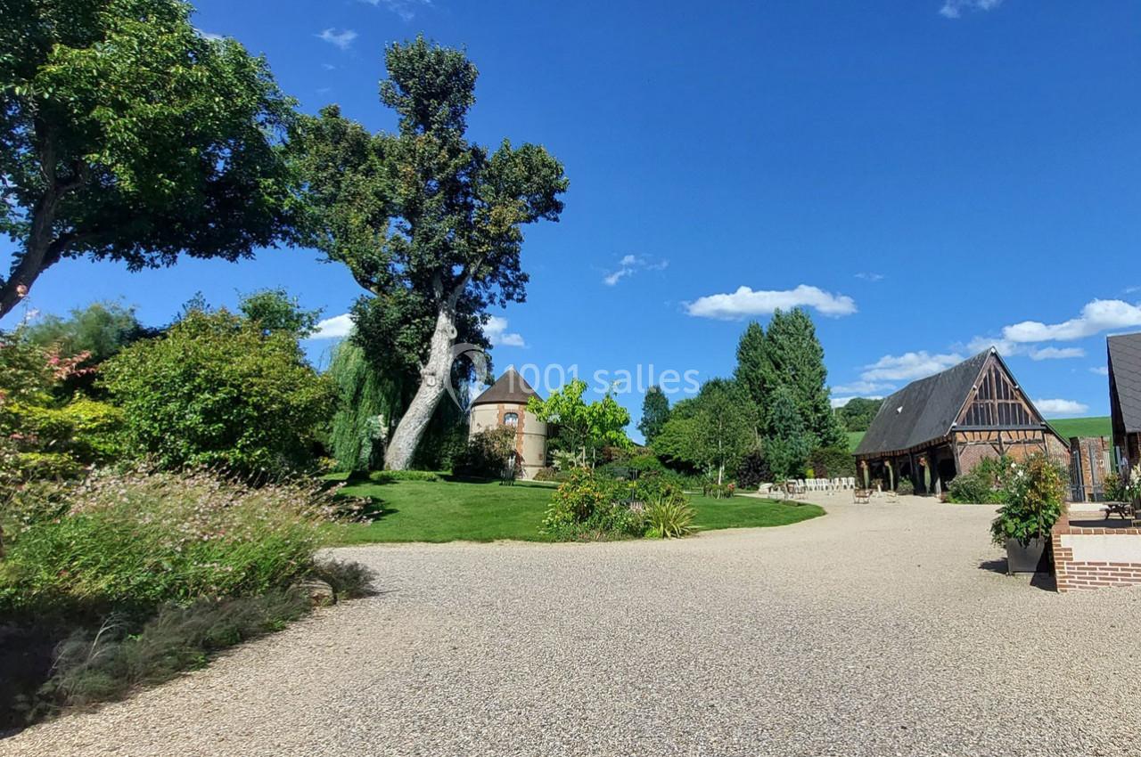 Cour extérieure avec allée gravillonnée, pelouse, arbres, et bâtiments en bois sous un ciel bleu dégagé.