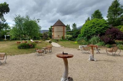 Jardin avec bancs, tables en bois et un pigeonnier en arrière-plan sous un ciel nuageux.