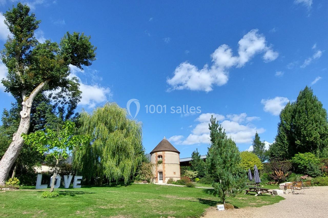 Jardin verdoyant avec un petit bâtiment rond, des arbres, des lettres ’LOVE’ et des tables de pique-nique sous un ciel bleu.