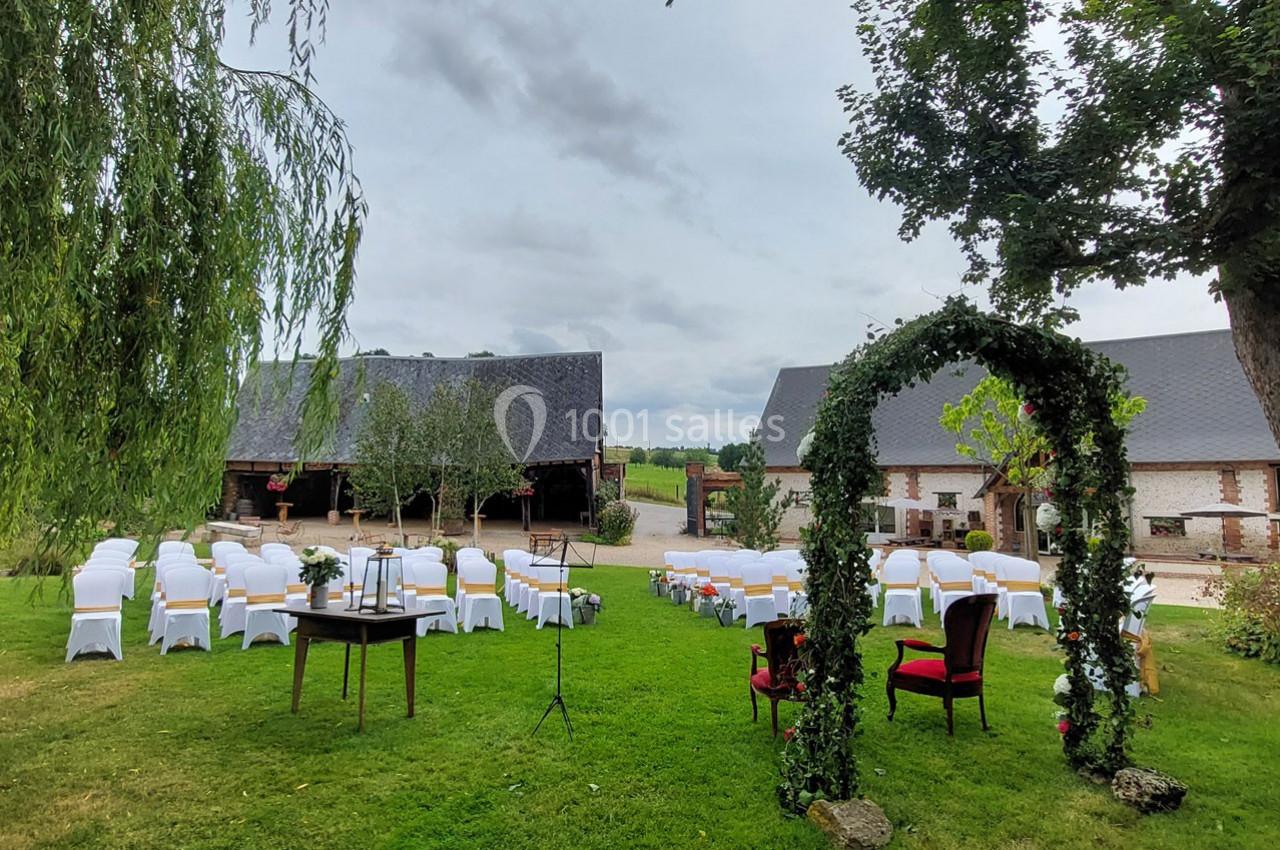 Chaises blanches disposées en extérieur devant une arche végétale, avec des bâtiments en briques et un ciel nuageux en…