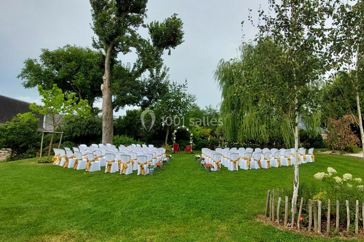 Chaises blanches décorées en cercle sur une pelouse, entourées d'arbres, préparées pour une cérémonie en plein air.
