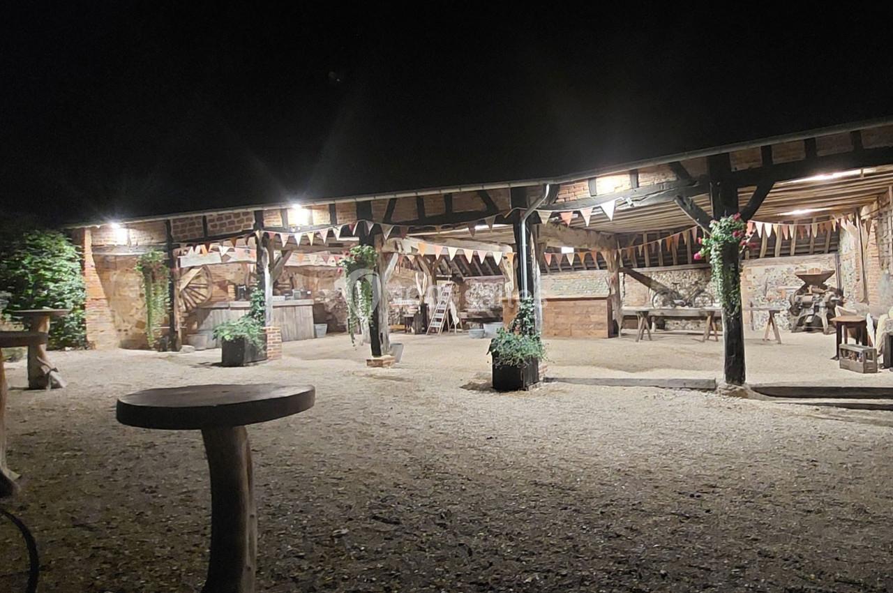 Cour extérieure éclairée la nuit avec une structure en bois ouverte, décorée de guirlandes et de plantes.