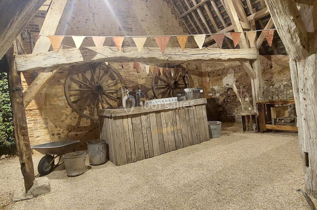 Intérieur d'une grange rustique avec un comptoir en bois, des guirlandes de fanions et des roues en arrière-plan.