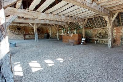 Jardin avec bancs, tables en bois et un pigeonnier en arrière-plan sous un ciel nuageux.