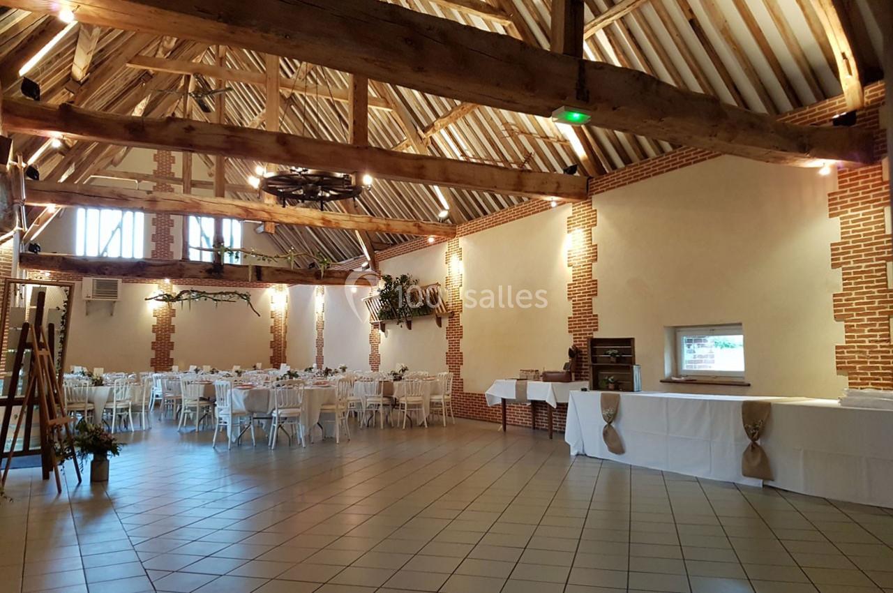 Salle de réception spacieuse avec poutres apparentes, tables dressées et décoration sobre.