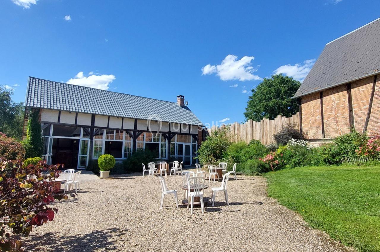 Cour extérieure avec tables et chaises blanches sur un sol gravillonné, entourée de bâtiments en briques et verdure.