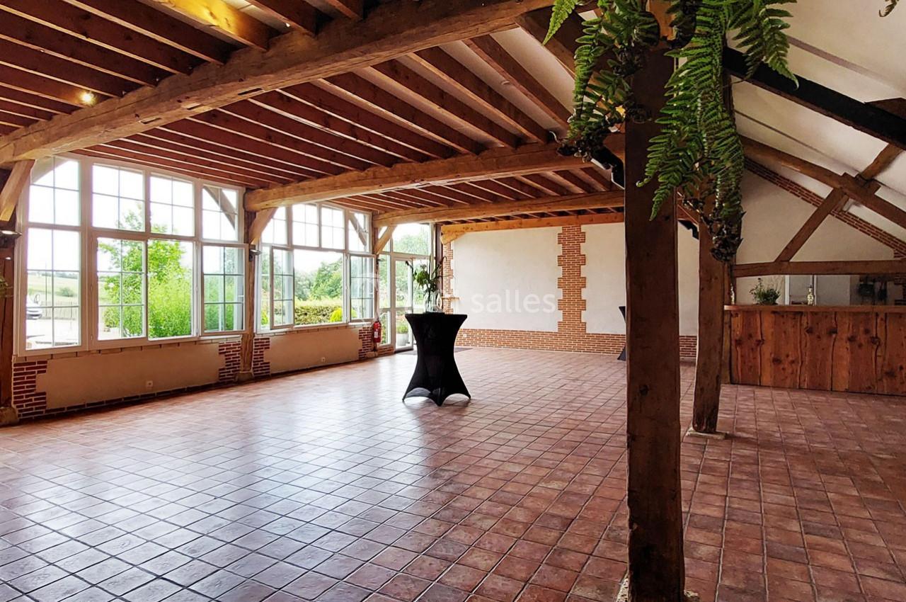 Salle lumineuse avec poutres apparentes, grandes fenêtres, sol en carrelage et comptoir en bois dans un cadre rustique.