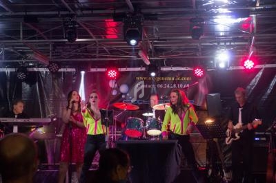 Un groupe de musique se produit sur scène avec des chanteuses et musiciens sous des éclairages colorés.