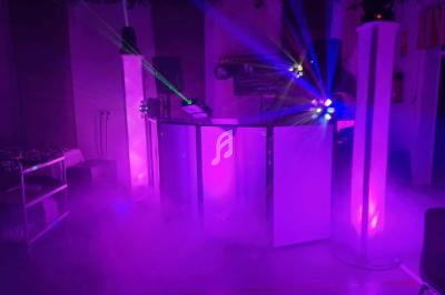 Jeune ambiance de fête avec lumières colorées, lasers et fumée autour d'une cabine de DJ.