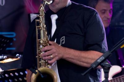 Un musicien joue du saxophone sur scène, accompagné d'un bassiste en arrière-plan.