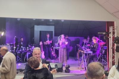 Un groupe de musiciens et une chanteuse se produisent sur scène dans une salle avec des spectateurs au premier plan.