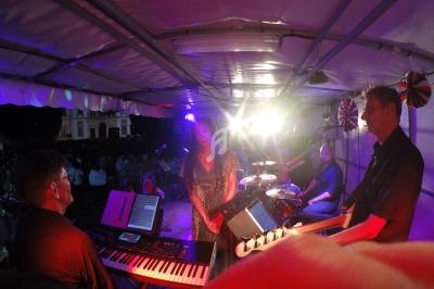 Musiciens jouant sur une scène éclairée, avec une chanteuse au centre et un public visible en arrière-plan.