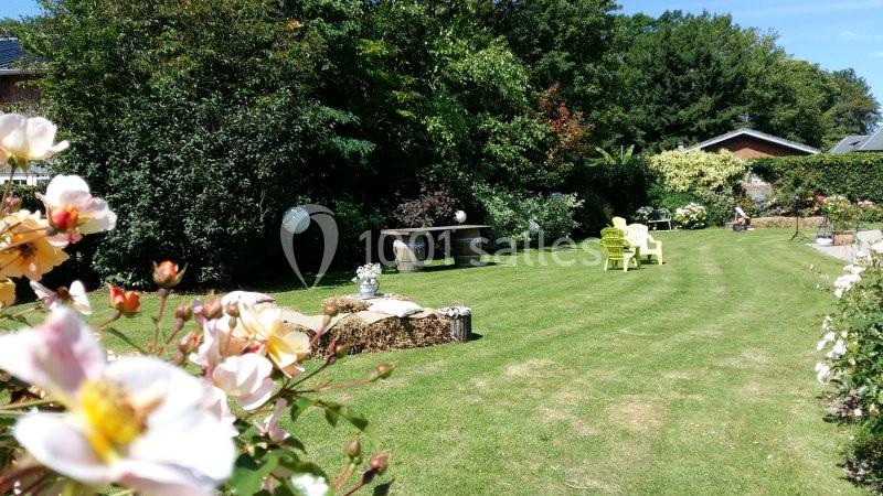 Jardin verdoyant avec pelouse, fleurs au premier plan, chaises et table en arrière-plan sous un ciel dégagé.
