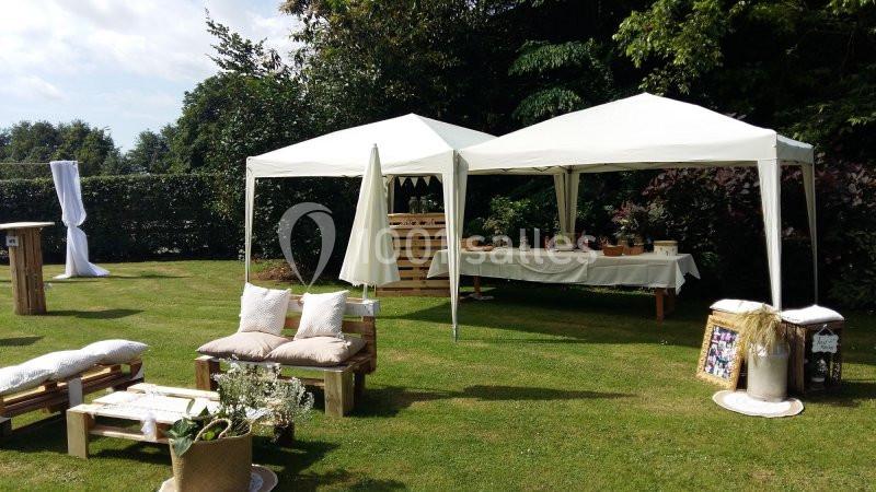 Tentes blanches installées dans un jardin, avec des tables décorées et des assises en palettes sur la pelouse.