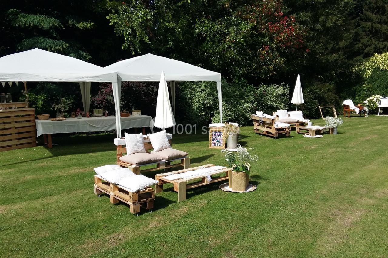 Mobilier en palettes avec coussins sous des tonnelles blanches dans un jardin verdoyant.