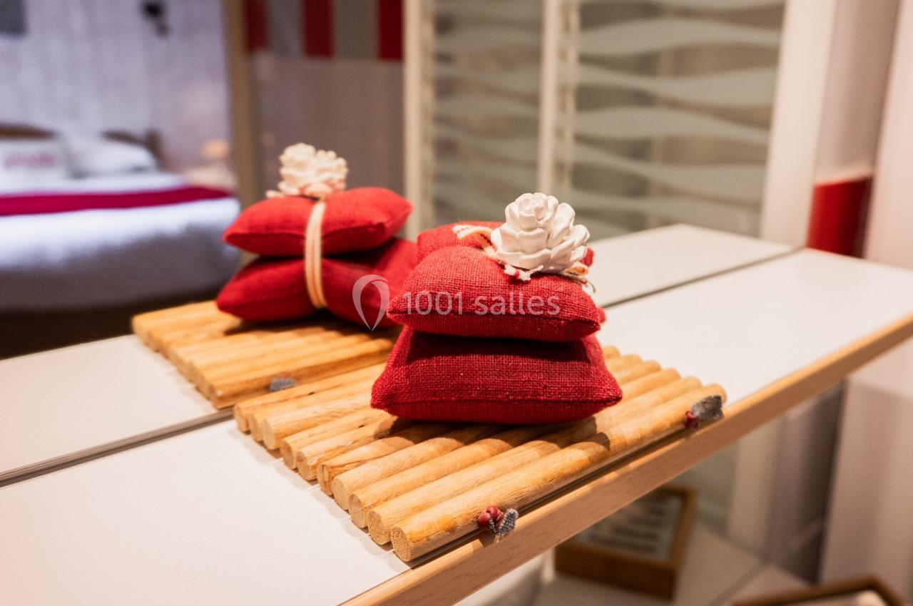 Deux coussins rouges décoratifs avec une fleur blanche, posés sur un support en bois devant un miroir.