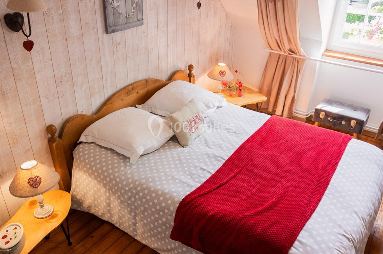 Lit double avec draps à motifs et couverture rouge, entouré de tables de chevet et éclairé par une fenêtre.