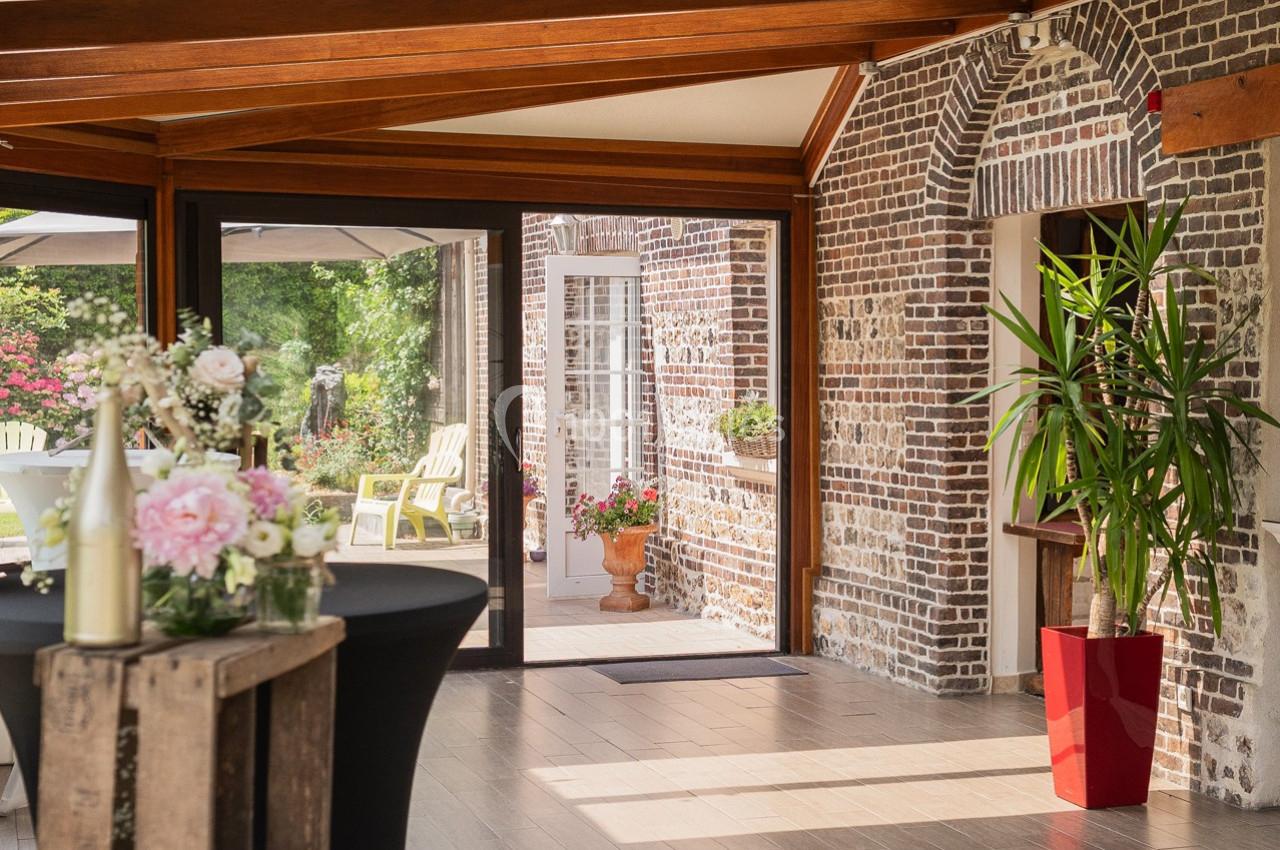Salle lumineuse avec murs en briques, grandes baies vitrées, plantes décoratives et vue sur un jardin fleuri.