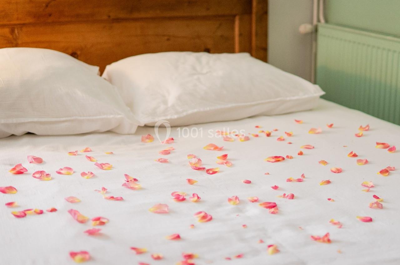 Pétales de rose éparpillés sur un lit avec des oreillers blancs et une tête de lit en bois.