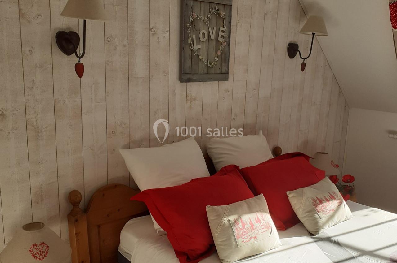 Lit double avec coussins rouges et décorations murales en bois, dans une chambre lumineuse au style rustique.