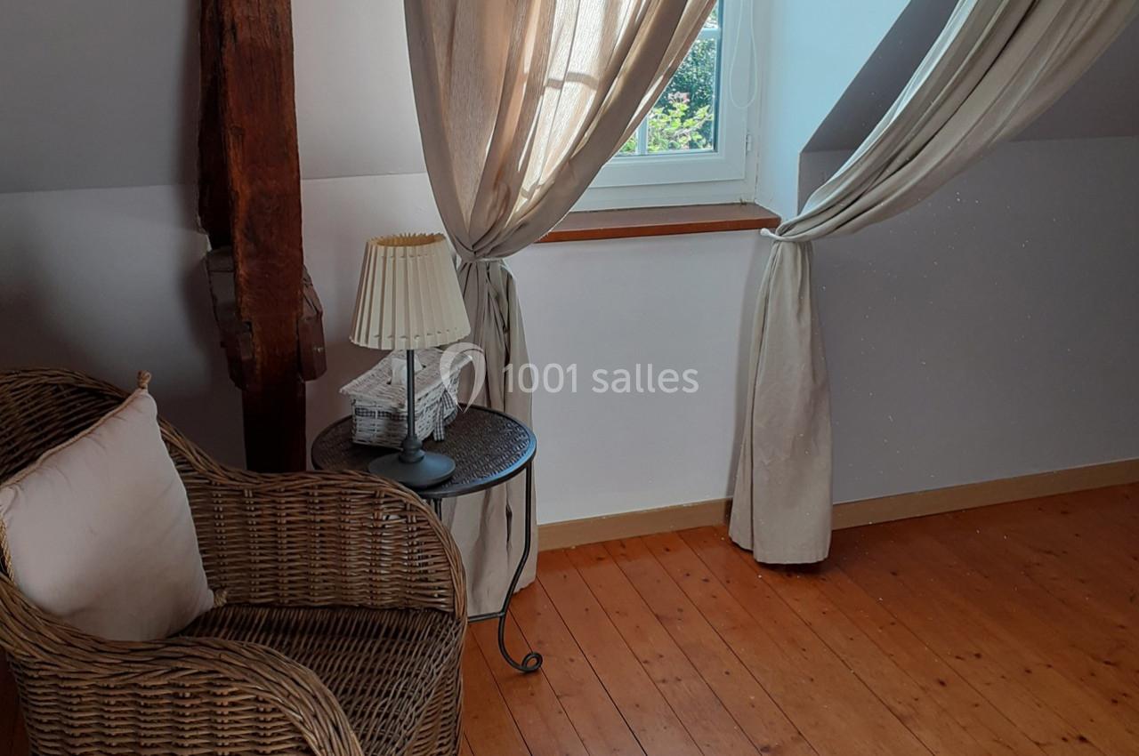 Fauteuil en osier avec coussin, table d'appoint et lampe près d'une fenêtre encadrée de rideaux clairs dans une pièce…