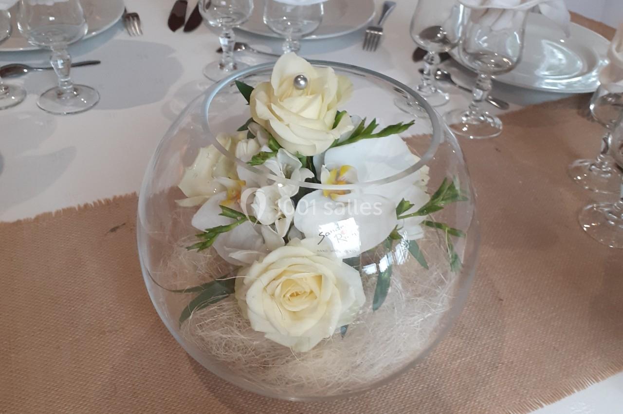 Centre de table avec roses blanches et fleurs dans un vase en verre rond, sur une nappe en toile de jute.