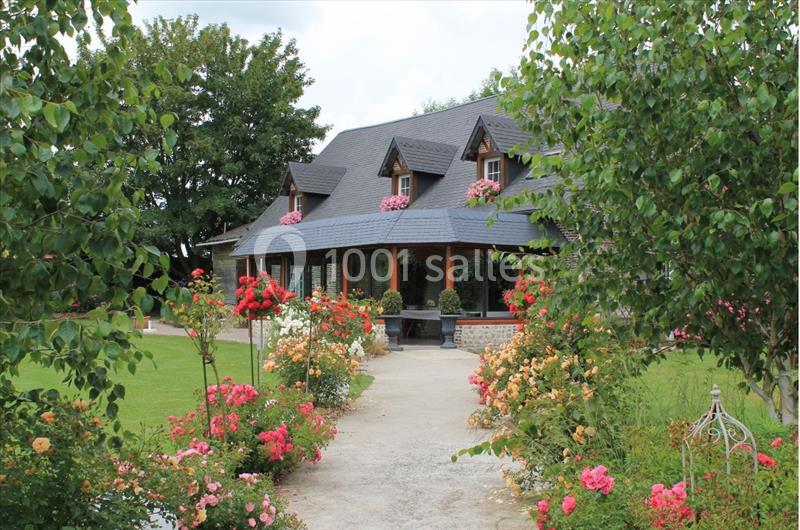 Maison en pierre avec toit en ardoise, entourée d'un jardin fleuri et d'arbres, par une journée ensoleillée.