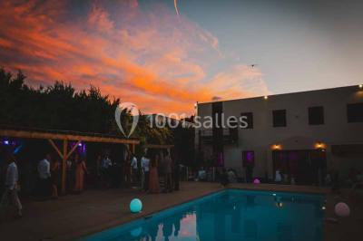 Une mariée lance son bouquet à un groupe de femmes rassemblées dans un jardin lors d'une réception en soirée.