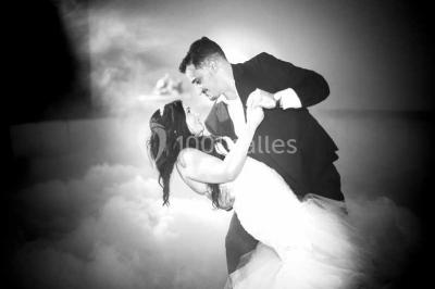 Une mariée lance son bouquet à un groupe de femmes rassemblées dans un jardin lors d'une réception en soirée.